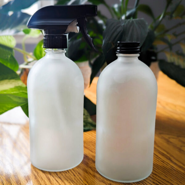 Two glass bottles with spray and screw on tops on a wooden table in front of plants